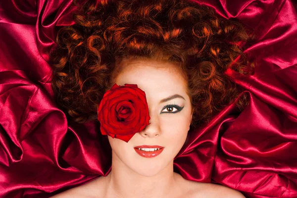 Donna dai capelli rossi con un fiore su uno sfondo di tende — Foto Stock