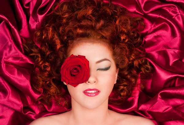 stock image Red-haired woman with a flower on a background of curtains