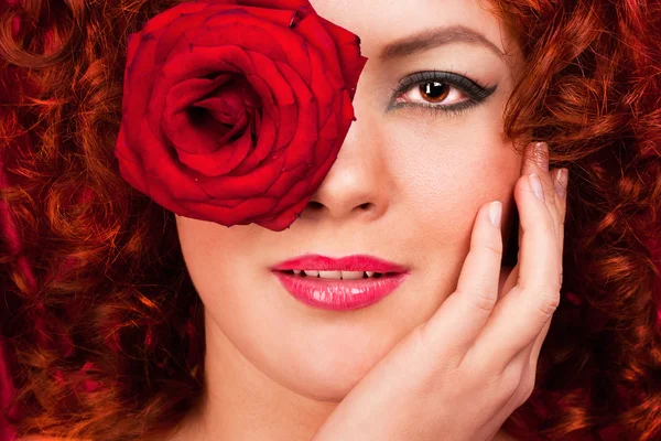 Donna dai capelli rossi con un fiore su uno sfondo di tende — Foto Stock