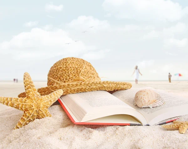 Sombrero de paja, libro y conchas marinas en la arena —  Fotos de Stock