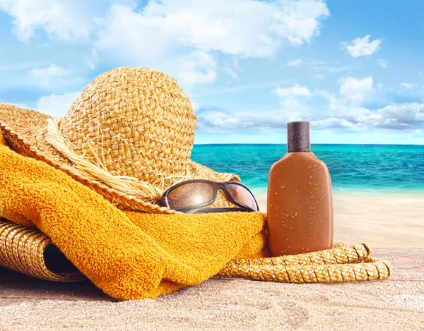 Zonnebrand lotion, stro hoed op het strand — Stockfoto