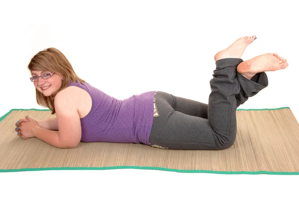 A young teenager in exercise pants lying on her stomach on a yoga matt on t...