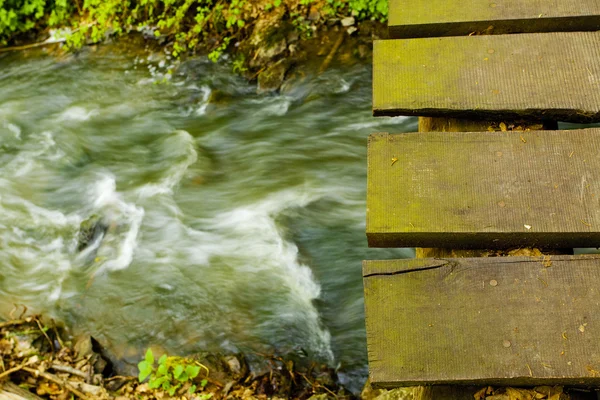 Ponte di legno su un torrente di montagna nel bosco — Foto Stock