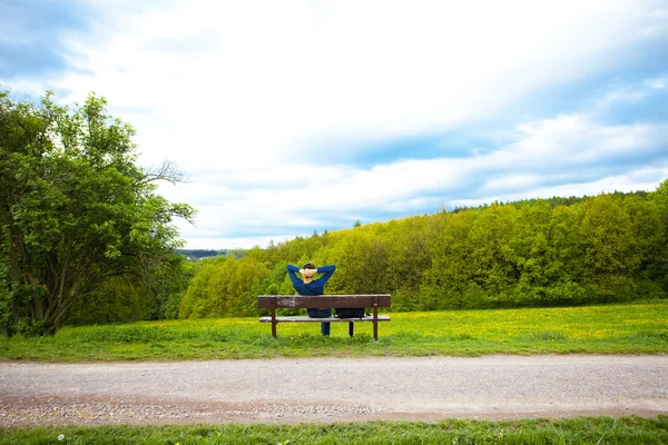 Mężczyzna odpoczynek na ławce na polu mniszek lekarski — Zdjęcie stockowe