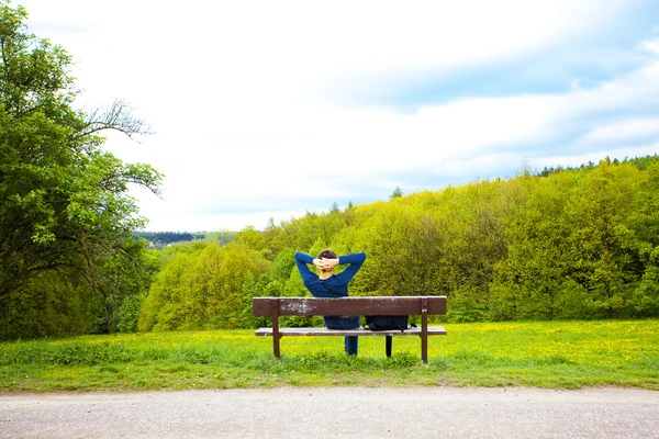 Dandelions alanında bankta oturan erkek — Stok fotoğraf
