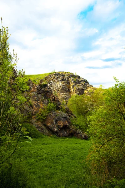 Скеля з зеленим на фоні блакитного неба з хмарами — стокове фото