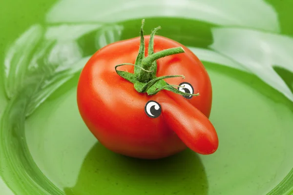 Tomato with a nose lying on the green dish — Stock Photo, Image