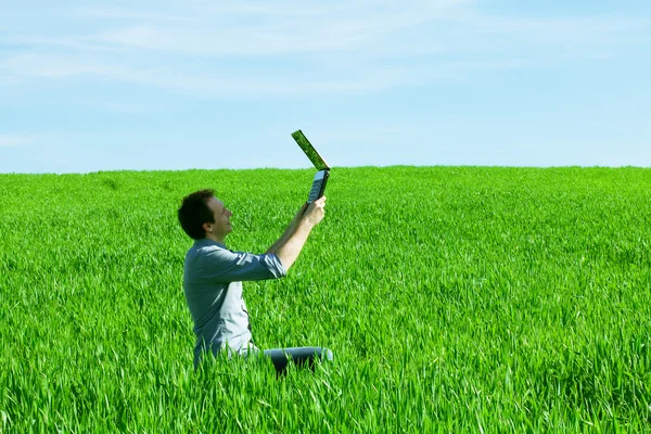 Young man uses a laptop in the green field — Stock Photo, Image