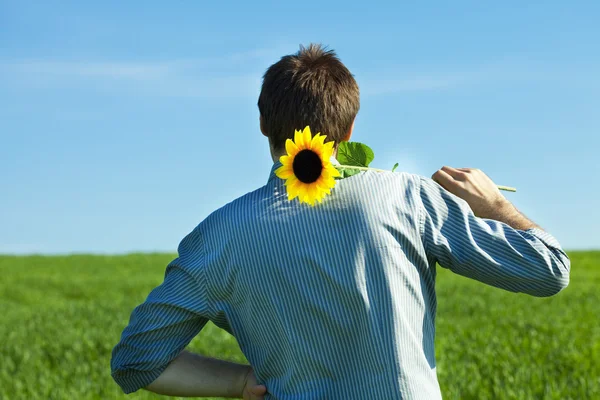 Junger Mann steht mit Sonnenblume auf der grünen Wiese — Stockfoto