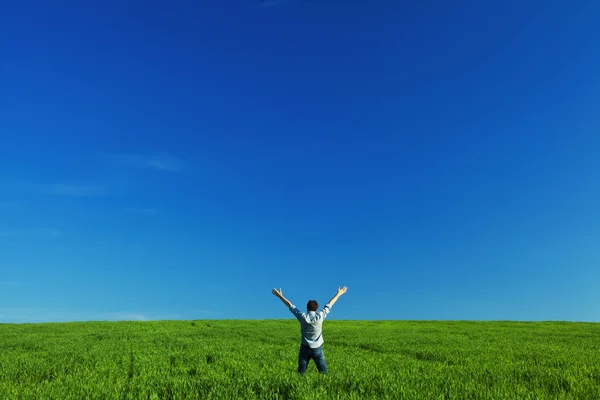 Ung man utsträckta armar i grönt fält mot den blå himlen — Stockfoto