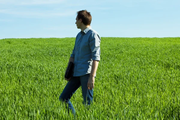 Giovane uomo in piedi con un computer portatile nel campo verde — Foto Stock