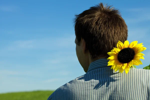 Νεαρός άνδρας στέκεται με ένα ηλιοτρόπιο στο πράσινο πεδίο — Φωτογραφία Αρχείου