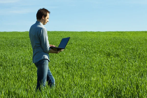 Jovem usa um laptop no campo verde — Fotografia de Stock