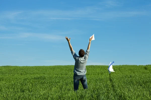 在绿色的原野中投掷纸张的年轻人 — 图库照片