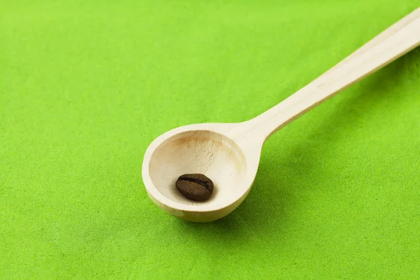 Granos de café en una cuchara de madera sobre un fondo verde —  Fotos de Stock