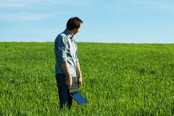 Jonge man met laptop in het veld — Stockfoto