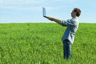 Young man using laptop in the field clipart