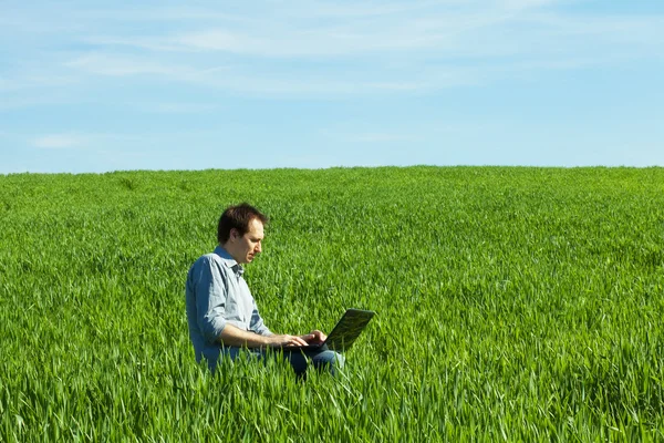 Νεαρός άνδρας, χρησιμοποιώντας φορητό υπολογιστή στο πεδίο — Φωτογραφία Αρχείου