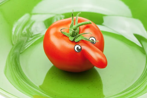 Tomate mit Nase auf grünem Teller — Stockfoto