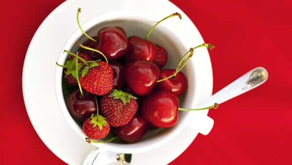 Tasse Untertassenlöffel Kirsche und Erdbeere auf rotem Hintergrund — Stockfoto