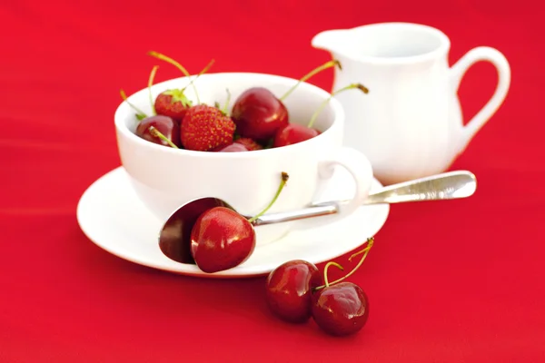 Молочный кувшин блюдце ложка вишня и клубника на красной backgro — стоковое фото