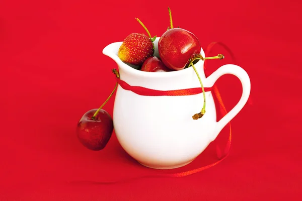 ミルク水差しリボン チェリーとイチゴを赤の背景 — ストック写真