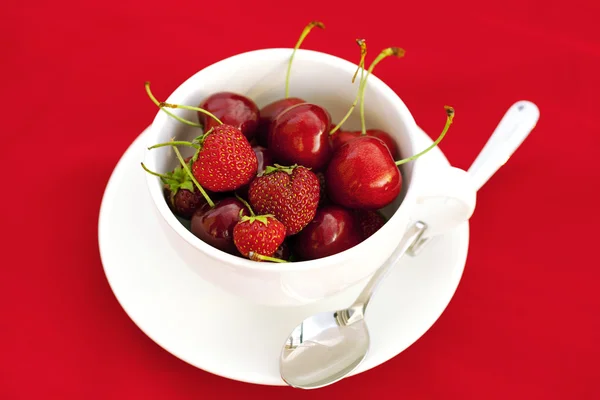 Kopje schotel lepel cherry en aardbei op een rode achtergrond — Stockfoto