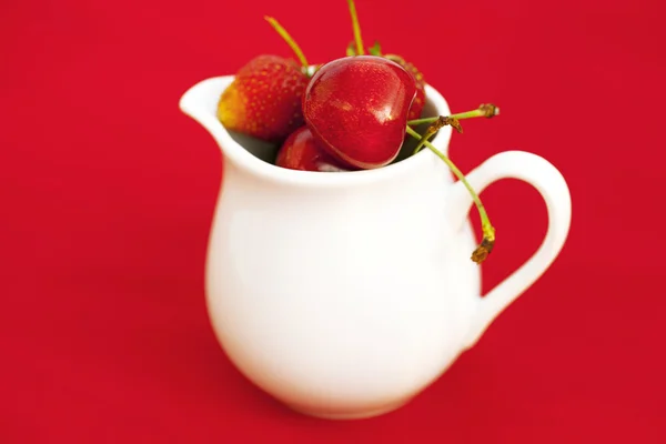 Jarra de leche cereza y fresa sobre un fondo rojo — Foto de Stock