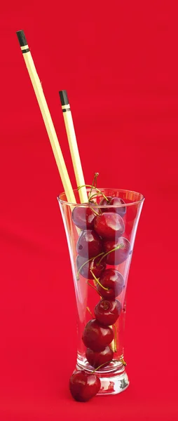 Vaso con cerezas y con palillos sobre fondo rojo — Foto de Stock