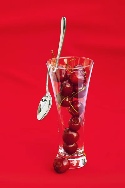 Glas van cherry en lepel op een rode achtergrond — Stockfoto
