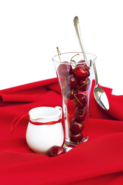Jarra de leche con un vaso de cinta de cereza y cuchara en un respaldo rojo —  Fotos de Stock