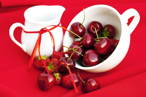 Melkkannetje met een lint kersen en aardbeien in een witte kop — Stockfoto