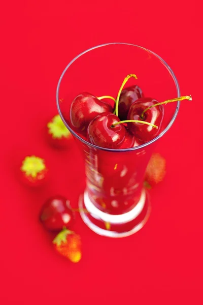 Verre de cerise et de fraise sur fond rouge — Photo