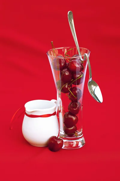 Krabice od mléka se sklenkou stuha cherry a lžící na červené pozadí — Stock fotografie
