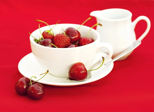Milchkännchen-Tasse Untersetzerlöffel Kirsche und Erdbeere auf rotem Backblech — Stockfoto