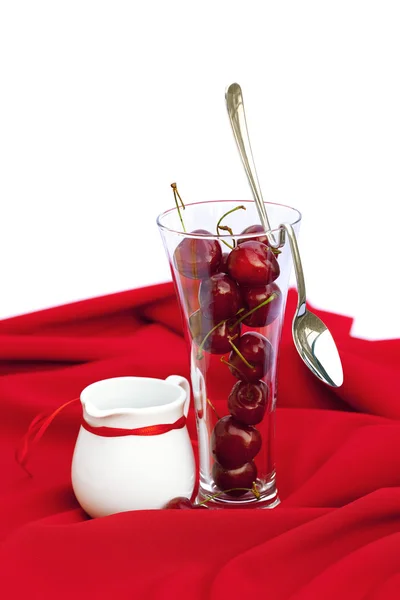 Jarra de leche con un vaso de cinta de cereza y cuchara en un respaldo rojo — Foto de Stock