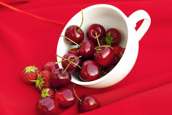 Cerezas y fresas en una taza blanca sobre un fondo rojo — Foto de Stock