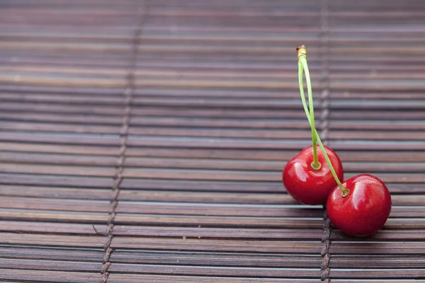 Two cherries in plate on a bamboo mat — Stock Photo, Image
