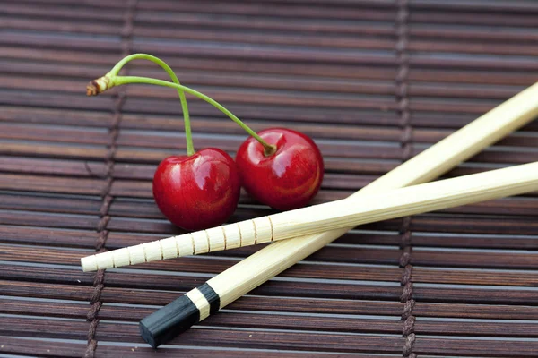 Вишня и палочки для еды на бамбуковом коврике — стоковое фото