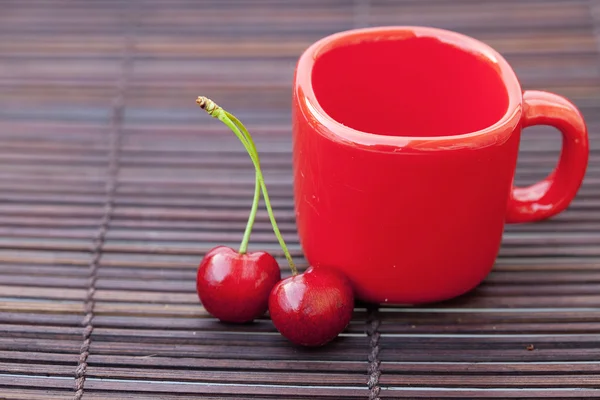 Cherry and cup on bamboo mat — Stock Photo, Image