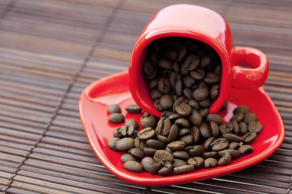 Taza y platillo y granos de café en una estera de bambú — Foto de Stock