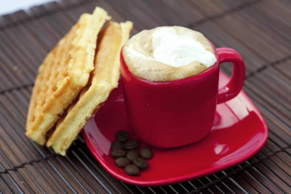 Чашка капучино вафель і кавових зерен на бамбуковому килимку — стокове фото