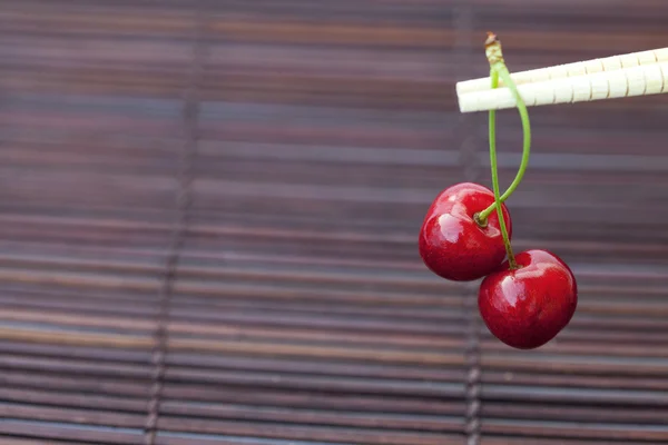 Cherry and chopsticks on bamboo mat — Stok fotoğraf