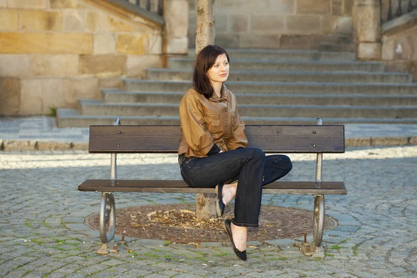 Piękna młoda kobieta siedzi na ławce — Zdjęcie stockowe