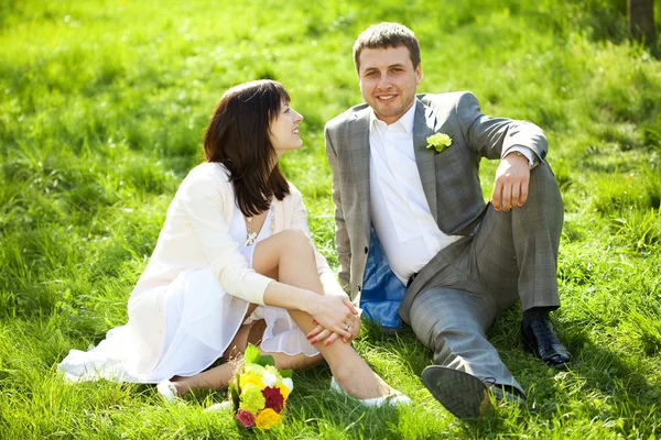 Только что поженились в цветочном саду, сидя на траве — стоковое фото