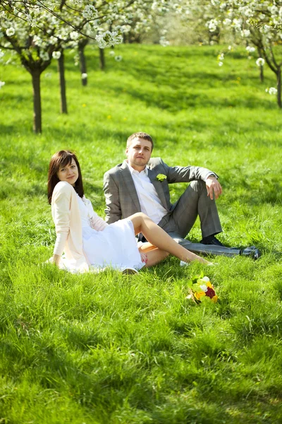 Recién casada en un jardín floreciente sentada en la hierba —  Fotos de Stock