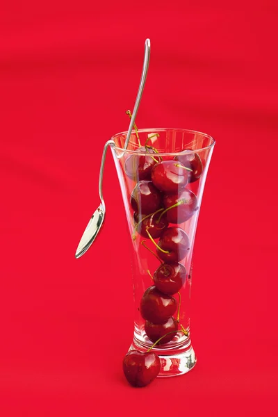 Vaso de cereza y cuchara sobre fondo rojo — Foto de Stock