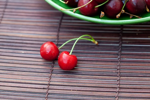 Two cherries in plate on a bamboo mat — Stok fotoğraf