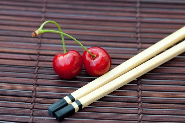 Вишня и палочки для еды на бамбуковом коврике — стоковое фото