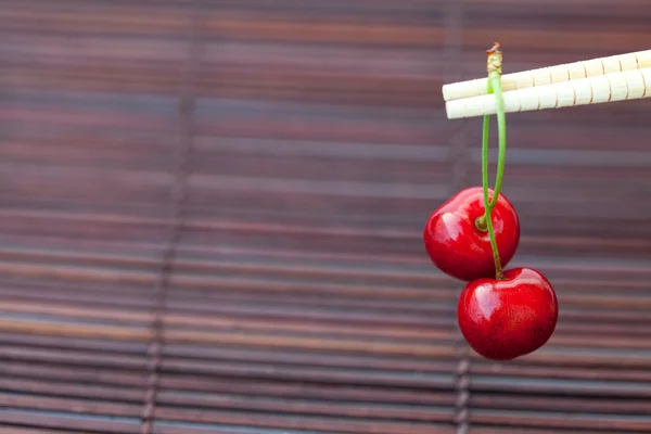 Cherry and chopsticks on bamboo mat — Stok fotoğraf